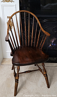 Front angled view of antique Windsor wooden chair showing curved spindle backrest and rounded armrests.