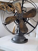 Front view of antique General Electric metal fan with four blades and protective wire cage, showing GE logo
