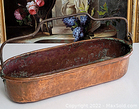Side view of antique copper bucket showing hammered texture and handle extending across the top.