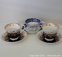 Three cups and saucers: two black and gold Royal Albert sets and one blue and gold Coalport set shown together.