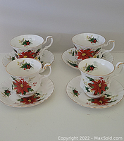 Four Royal Albert cups and matching saucers with a Christmas poinsettia and holly floral pattern, arranged in two pairs.