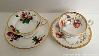 Two porcelain tea cup and saucer sets displayed side by side showing their floral designs and gold trim.