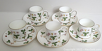 Set of 5 demitasse cups and 5 matching saucers arranged on a surface showing the floral and leaf pattern with gold rims and handles.