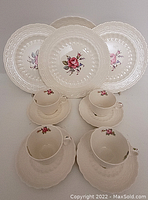 Full set of dessert plates, teacups, and saucers arranged in rows showing embossed detail and floral design.