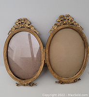 Open hinged double picture frame showing front and inside of brass frames with ornate detail and glass covering.