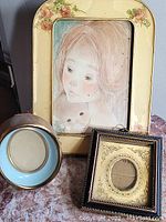 Three photo frames: one rectangular floral design with portrait, a small round blue one, and a square dark wood with gold matting.