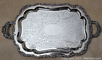 Full view of the silver plated tray laid flat on carpet showing engraved surface and ornate handles with scalloped edges