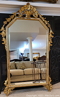 Full view of large gilt wood mirror leaning against fireplace showing overall dimensions and styling