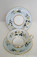 Cup, saucer and plate with yellow rose floral pattern and gold trim displayed against neutral background