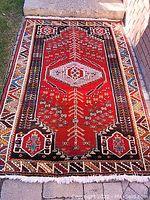 Full view of rectangular rug, red field with geometric motifs and fringed ends, displayed on concrete surface