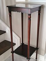 Front and side view showing the full height and design of the wooden plant stand with two square shelves and turned legs.