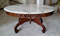 Side view of the coffee table showing carved floral wooden apron and legs supporting the marble top