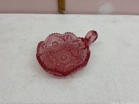 Pink pressed glass candy dish with detailed geometric and floral patterns, viewed from an angled side perspective.