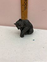 Bronze bear figurine shown from side with ruler indicating approximately 2 inches in size.