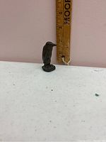 Side view of small bronze penguin figurine next to a ruler for scale showing height around 2 inches