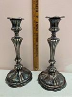 Full view of the two silver plated weighted candlesticks with scalloped bases and ornate stems, measured against a ruler showing about 8.5 inches height.