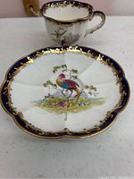 Porcelain saucer with bird painted in center and cobalt blue rim with ornate gold decoration