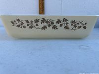 Side view showing decorative brown and gold leaf vine pattern on cream-colored Pyrex casserole dish.