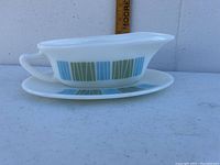 Side view of the white Pyrex gravy boat with blue and green vertical stripe decoration and matching underplate.