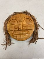 Top view of the carved wooden mask showing detailed facial features and natural fiber accents.