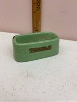 Photo of miniature green enameled bathtub with partial label visible and measuring stick behind it