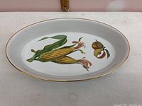 Oval white porcelain dish with corn and apple vegetable illustrations and gold rim.