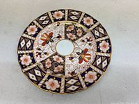 Top view of the Royal Crown Derby porcelain saucer showing elaborate floral and geometric patterns in blue, gold, white, and reddish-orange.