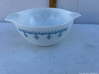 White Pyrex mixing bowl with blue snowflake garland pattern, shown from side angle highlighting the design and shape with spouts.