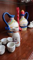 Hand-painted ceramic cruets, sake bottle, and sake cups on wooden surface