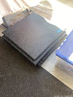 Stack of five black speckled foam mats on gym flooring, showing top surfaces with blue and white flecks