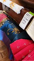 Multiple folded linens arranged on a wooden chest, showing blue, red, and white fabrics with various patterns and embroidery including sunflowers.
