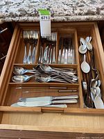 Drawer with organized metal forks, spoons, knives, butter spreaders, and chopsticks on the right side along with white porcelain tasting spoons.