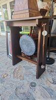 Side angled view of the dinner gong hanging inside a wooden stand. The mallet is hanging on the right side of the stand.