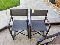 Front view of two dark metal folding patio chairs with black mesh seats and backs side by side.