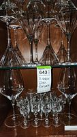 Two wood shelves filled with assorted glass barware including wine glasses, martini glasses, and small glasses with long stems.