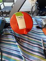 Front view of the red drum of the drain snake showing label and electrical cord plug on table with striped cloth background