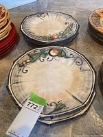 Six beige ceramic plates stacked, decorated with hand-painted fruit and green leaf motifs and dark blue rim accents.