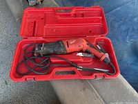 Milwaukee Sawzall reciprocating saw with power cord inside red carrying case. Two saw blades included.