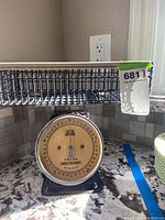 Front view of metal CCI kitchen scale with wire basket showing dial and scale capacity.