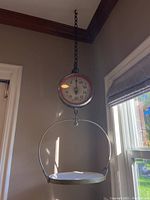 Full view of hanging scale mounted from ceiling chain with metal pan below dial