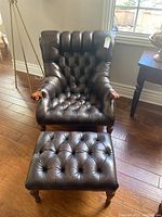 Front view of brown leather tufted chair with ottoman showing overall condition and design