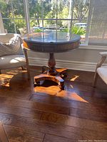 Full view of round vintage solid wood game table with pedestal base and four curved legs ending in caster wheels.