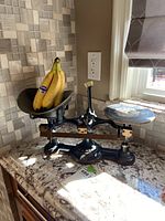 Full view of vintage black cast iron Troemner balance scale with bananas in the weighing pan to show size and setup.