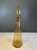 Amber glass genie decanter bottle with bulb-shaped stopper, standing against a neutral background.
