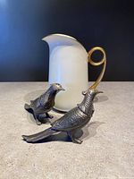 Front angle of beige ceramic pitcher with gold handle and two silver metal pheasant salt and pepper shakers