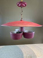 Full view of the red atomic saucer ceiling light hanging, showing the large flat metal shade and the three glass inserts below.