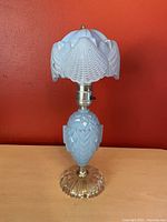 Full view of the blue art deco boudoir lamp showing the textured glass base, brass accents, and clamshell glass shade against an orange background.
