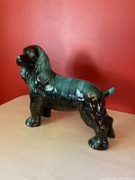 Side profile view of Blue Mountain Pottery ceramic Cocker Spaniel figurine on wooden surface with red background.