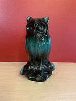 Front angle view of ceramic owl sculpture with dark brown, green glaze on red background.