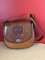 Front side of brown leather purse with monogram 'MA' and foliage design tooling. Turn lock closure visible.